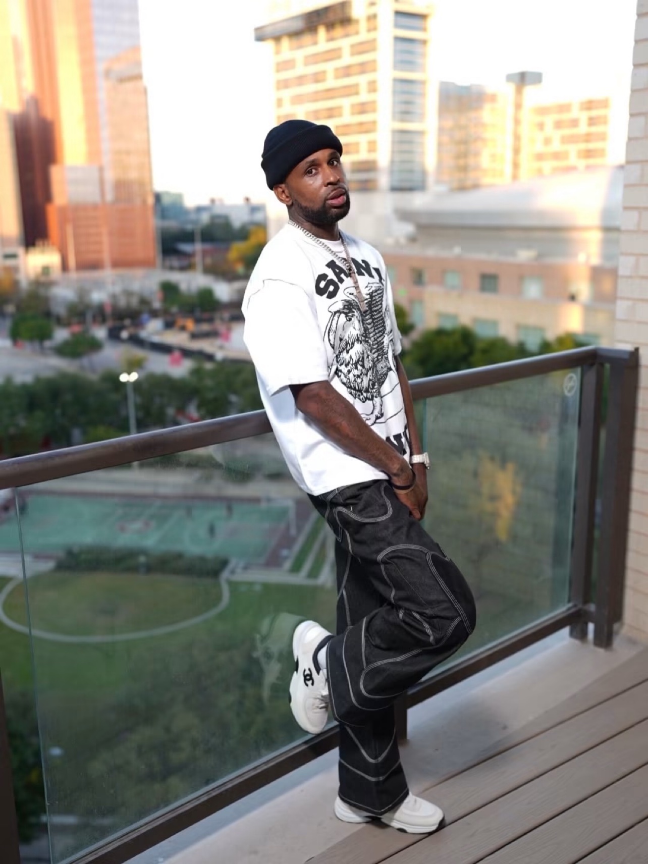 Bossman Yayo leaning on a balcony railing with a city skyline behind him
